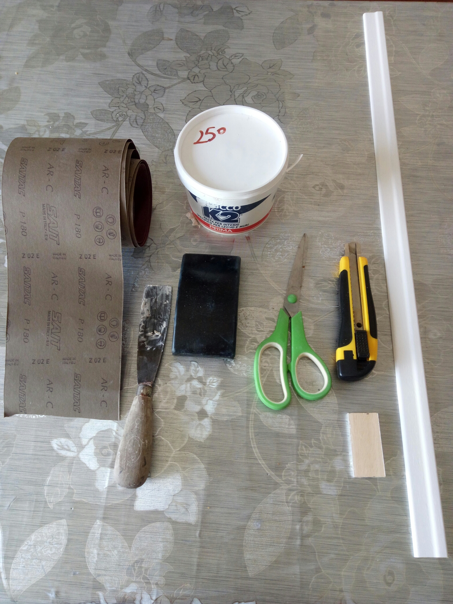 Carta abrasiva di tipo fine ma resistente;  Supporto gommato per carta abrasiva;  Cutter con lama grande professionale (taglierino);  Forbici;  Stucco per legno;  Metro;  Cornice a piacere.